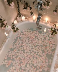 a bathtub filled with lots of flowers and candles next to some lights on the wall