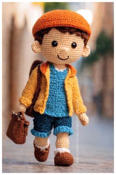 a small crocheted boy with a backpack and hat is walking down the street