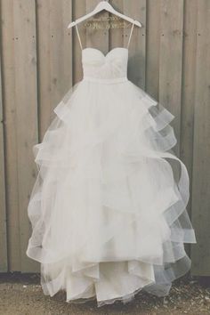 a wedding dress hanging on a hanger in front of a wooden wall with white paint