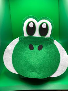 a green and white stuffed animal sitting on top of a green chair with big eyes