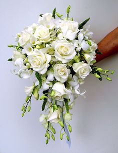 a bridal bouquet with white roses and greenery is held by a person's hand