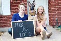 a man and woman sitting on the ground with a dog holding a sign that says our first home