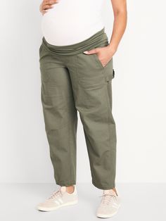 a pregnant woman in white shirt and khaki pants standing with her belly exposed