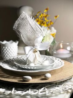 a table setting with white dishes and flowers in the vases on the plate are wrapped in burlap