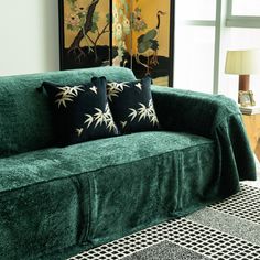 a green couch with two black and white pillows on top of it next to a lamp