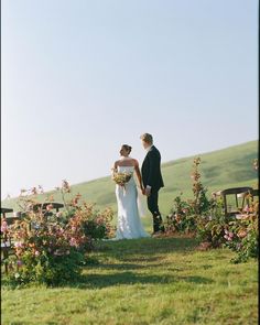 a bride and groom standing in the middle of a field with flowers on each side