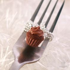 a chocolate cupcake sitting on top of a metal fork with chains attached to it