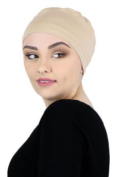 a woman wearing a beige turban and black top with her hair tied back