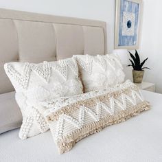 a white bed topped with pillows next to a potted plant