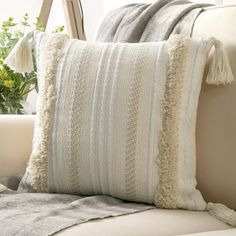 a close up of a pillow on a couch near a vase with flowers in it