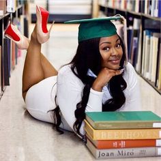 a woman laying on the floor in front of books wearing a graduation cap and gown