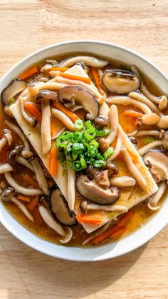 a white bowl filled with noodles and mushrooms on top of a wooden table next to a spoon