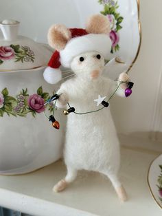 a white mouse with a christmas hat and lights on it's head holding a string