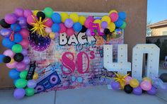 balloons and streamers decorate the backdrop for an 80's themed birthday party in front of a brick wall