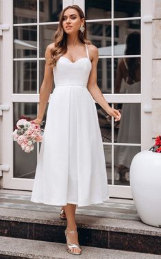 a woman in a white dress is standing on the steps with her hands behind her back