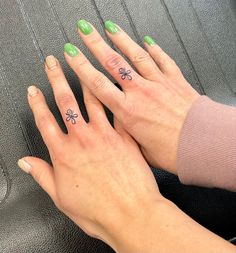 two hands holding each other with green fingernails and tattoos on their fingers, while sitting in a car