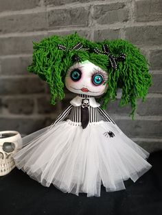 a doll with green hair and blue eyes wearing a white dress next to a skull