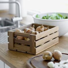 a wooden crate filled with onions on top of a counter next to a bowl of lettuce