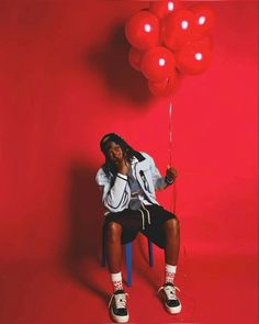 a woman sitting on a chair holding red balloons