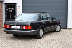 a black mercedes benz parked in front of a garage with a door open to the side