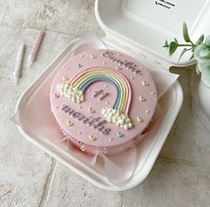 a pink cake with a rainbow on it in a plastic container next to a flower