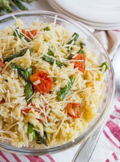 a glass bowl filled with pasta and veggies on top of a white table