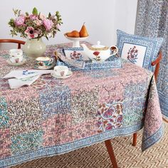 a table topped with tea cups and saucers covered in floral designs next to a vase filled with flowers