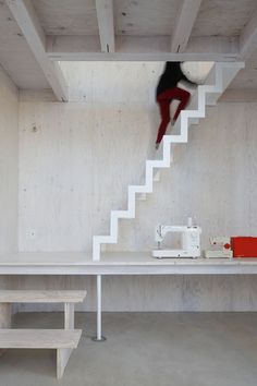 a woman is jumping down the stairs in a room with white walls and wood flooring