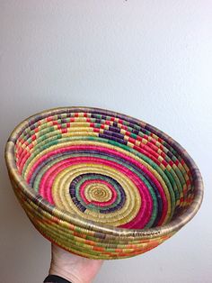 a hand holding a colorful woven bowl in front of a white wall