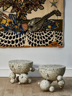 two stone stools sitting in front of a wall hanging