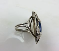 Circa 1910. Gorgeous Arts and Crafts Era ring in Sterling Silver with applied Oak leaves in magnificent detail on a hammered silver top. The center stone is a beautiful blue color and is probably Sodalite. The ring is a split shank design. Ring measurements (approximate) are as Antique Cabochon Sapphire Ring, Blue Cabochon Rings Art Deco Style, Art Deco Blue Cabochon Rings, Blue Art Deco Rings With Cabochon, Blue Cabochon Art Deco Rings, Vintage Silver Turquoise Ring For Wedding, Vintage Silver Turquoise Ring For Formal Occasions, Antique Silver Opal Ring, Antique Sapphire Ring With Polished Finish