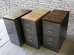 three metal filing cabinets sitting next to each other on top of a cement floor in front of a brick wall