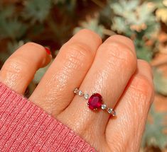 a woman's hand holding a ring with a red and white diamond on it