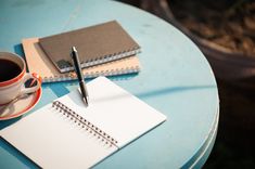 a cup of coffee, notebook and pen on a blue table