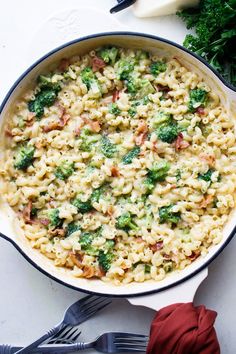 a casserole dish with broccoli and pasta in it next to silverware