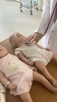 an adult doctor examines a dummy lying on the floor next to two children's dolls