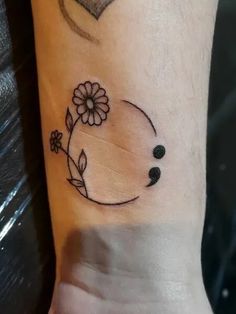 a small tattoo on the wrist of a woman with flowers and hearts around her neck