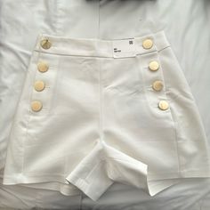 Elevate Your Wardrobe With These Stunning High-Rise Shorts That Exude Old Money Elegance. Crafted With A Premium Fabric Blend, These Shorts Feature A Flattering High-Waisted Silhouette And Eye-Catching Gold Button Detailing That Adds A Touch Of Sophistication. Designed To Flatter Your Figure, The High-Rise Waist Cinches At The Smallest Part Of Your Midsection, Creating A Sleek And Streamlined Look. The Fabric Is Soft, Breathable, And Slightly Stretchy For All-Day Comfort. Perfect For Dressy Casu Elegant High-waisted Shorts With Button Closure, Elegant High Waist Shorts With Button Closure, Elegant Shorts With Buttons, Elegant Short Bottoms With Button Closure, Elegant Short Bottoms With Buttons, Chic Summer Shorts With Button Cuffs, Elegant Buttoned Shorts For Spring, White High Waist Shorts With Buttons, Fitted White Shorts With Buttons