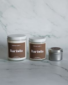 two jars of candles sitting on top of a marble counter