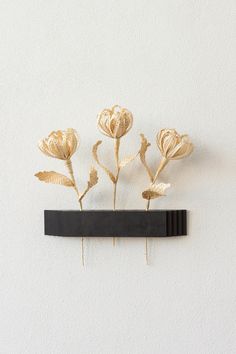 three gold flowers on a black shelf against a white wall