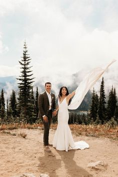 a man and woman standing on top of a mountain holding a white scarf in their hands