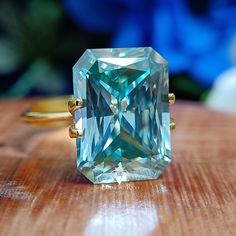 an aqua colored diamond ring sitting on top of a wooden table