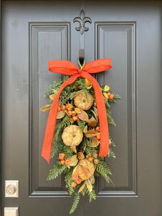 a wreath on the front door with an orange bow hanging from it's side