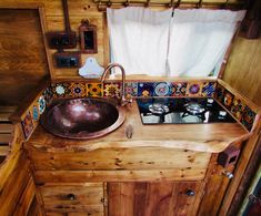 a sink in a wooden kitchen with colorful tiles on the counter top and window behind it