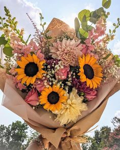 a bouquet of sunflowers and other flowers is wrapped in brown paper with a bow