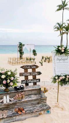 a wooden sign sitting on top of a sandy beach next to flowers and palm trees