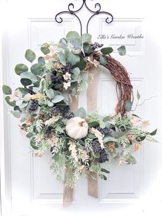 a wreath is hanging on the front door with greenery and pumpkins in it