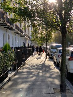 people are walking down the sidewalk in front of parked cars and apartment buildings on a sunny day