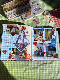 an open scrapbook with pictures and stickers on it sitting on a green tablecloth