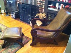 a living room with a chair, ottoman and bookcase in front of a fireplace